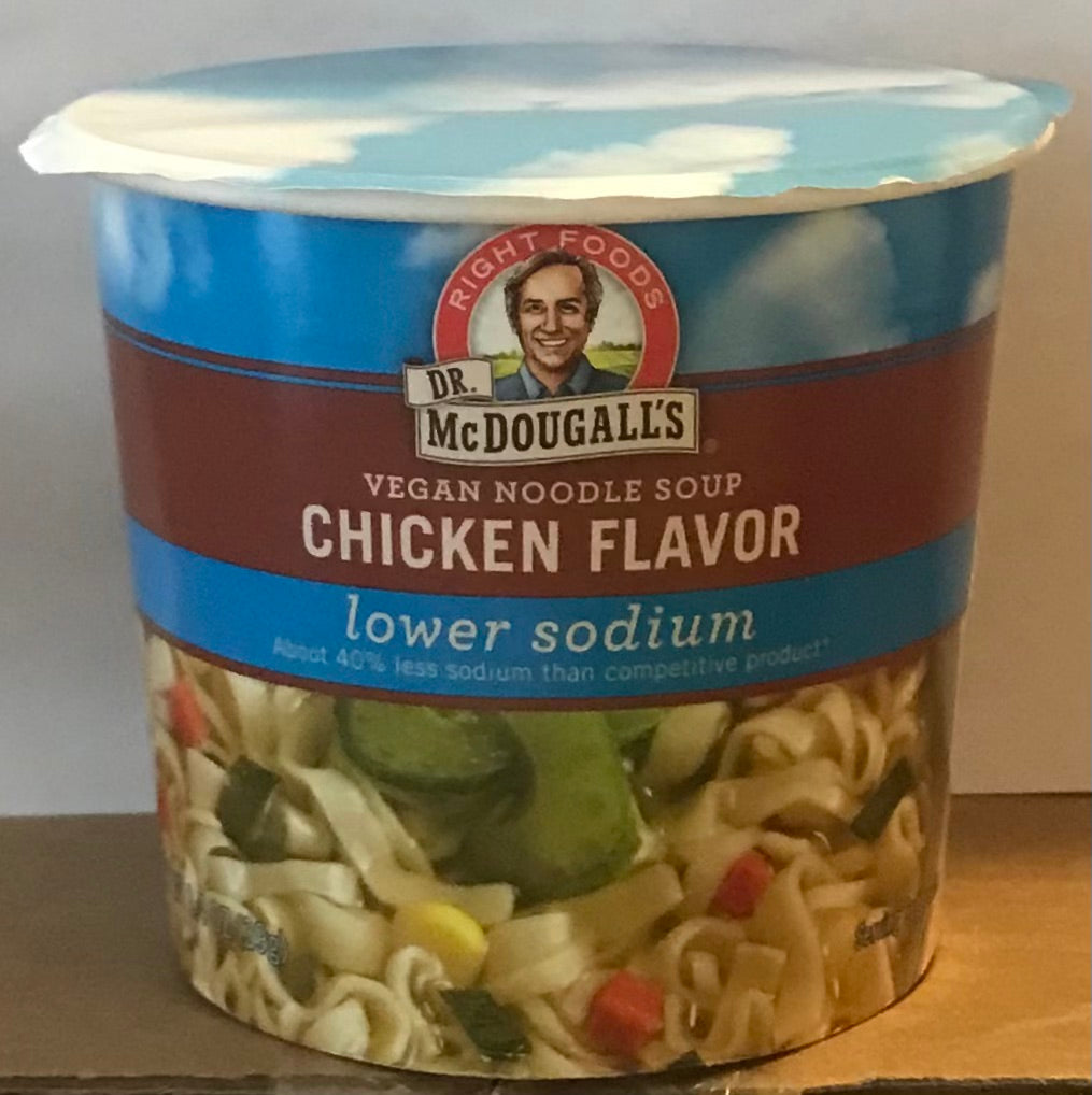 A container of Dr. McDougald's Vegan Noodle Soup, Chicken Flavor, lower sodium, with a blue lid and a label showing the brand logo and a picture of noodles with vegetables.